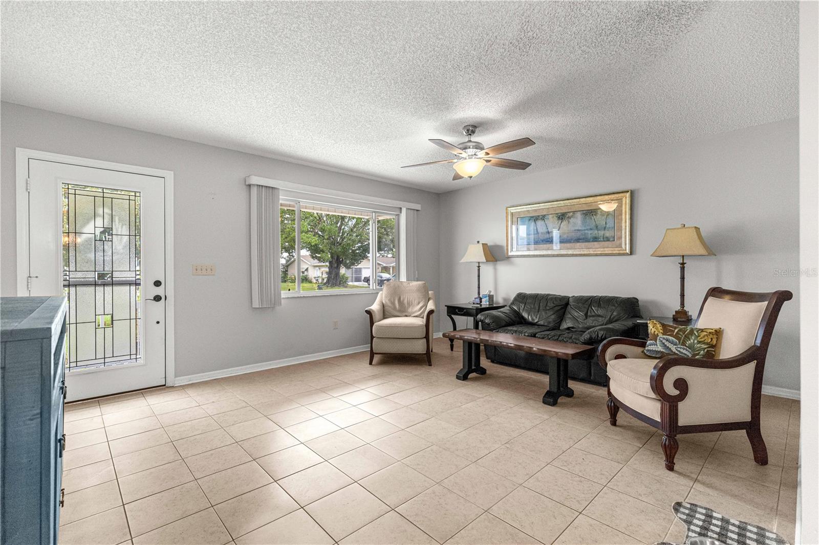 LIVING ROOM TO FRONT DOOR AND WINDOW DISPLAYING TILED FLOOR AND NEWER FAN