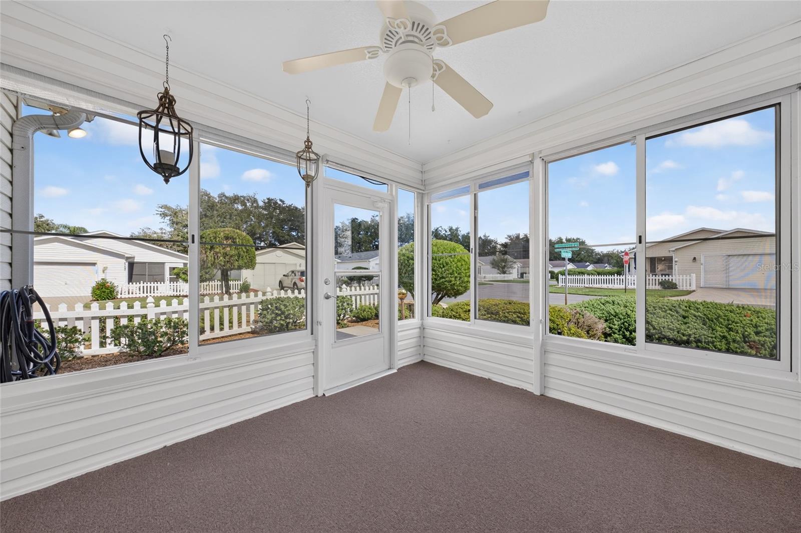 ENCLOSED LANAI - Plexiglass windows surround a bright sitting area with a ceiling fan and offers views of the landscaping and the corner of Escobar Ave & Elana Place.