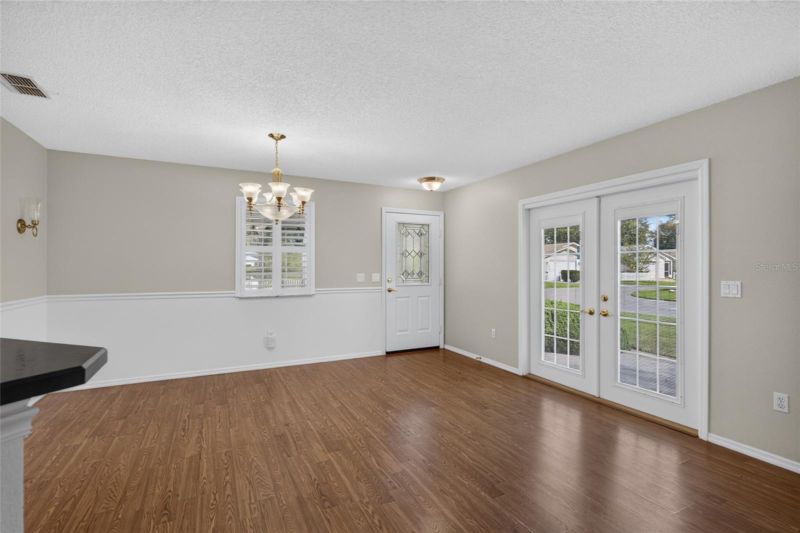 Close up view of DINING ROOM - Chair rail woodwork, decorative wall sconces (back L), and matching chandelier & pendant lighting add distinctive detail. Note the French doors which access the side patio on eastern side of home.