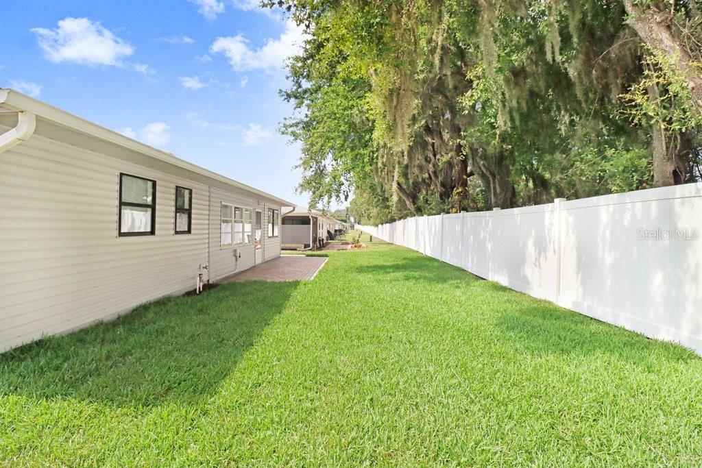 Back yard bordered by rear fence. Neighboring trees provide shade.