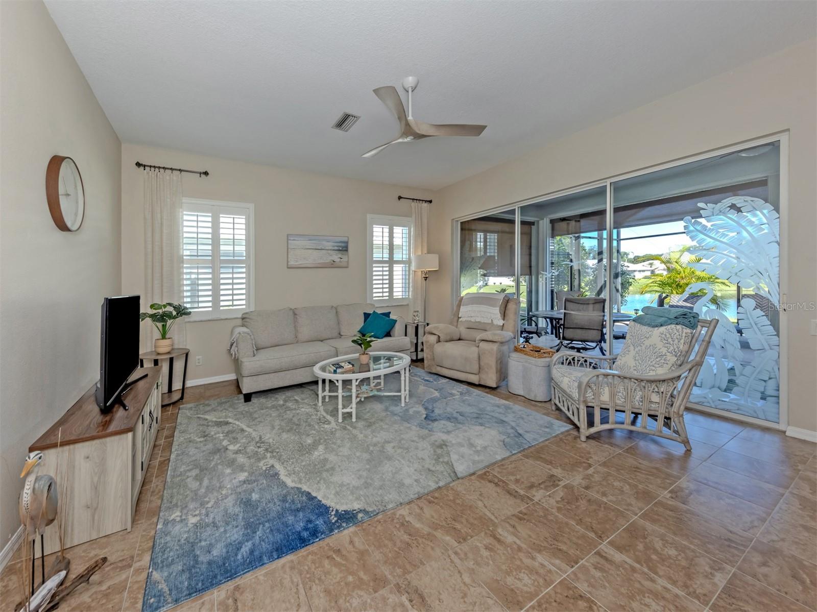 A spacious, inviting living room featuring beautiful, seamless ceramic tile flooring and elegant plantation shutters throughout the home, along with stunning etched-glass sliding doors opening to the extended lanai, bringing the beauty of the outdoors right into view! A spacious, inviting living room featuring beautiful, seamless ceramic tile flooring and elegant plantation shutters throughout the home, along with stunning etched-glass sliding doors opening to the extended lanai, bringing the beauty of the outdoors right into view!