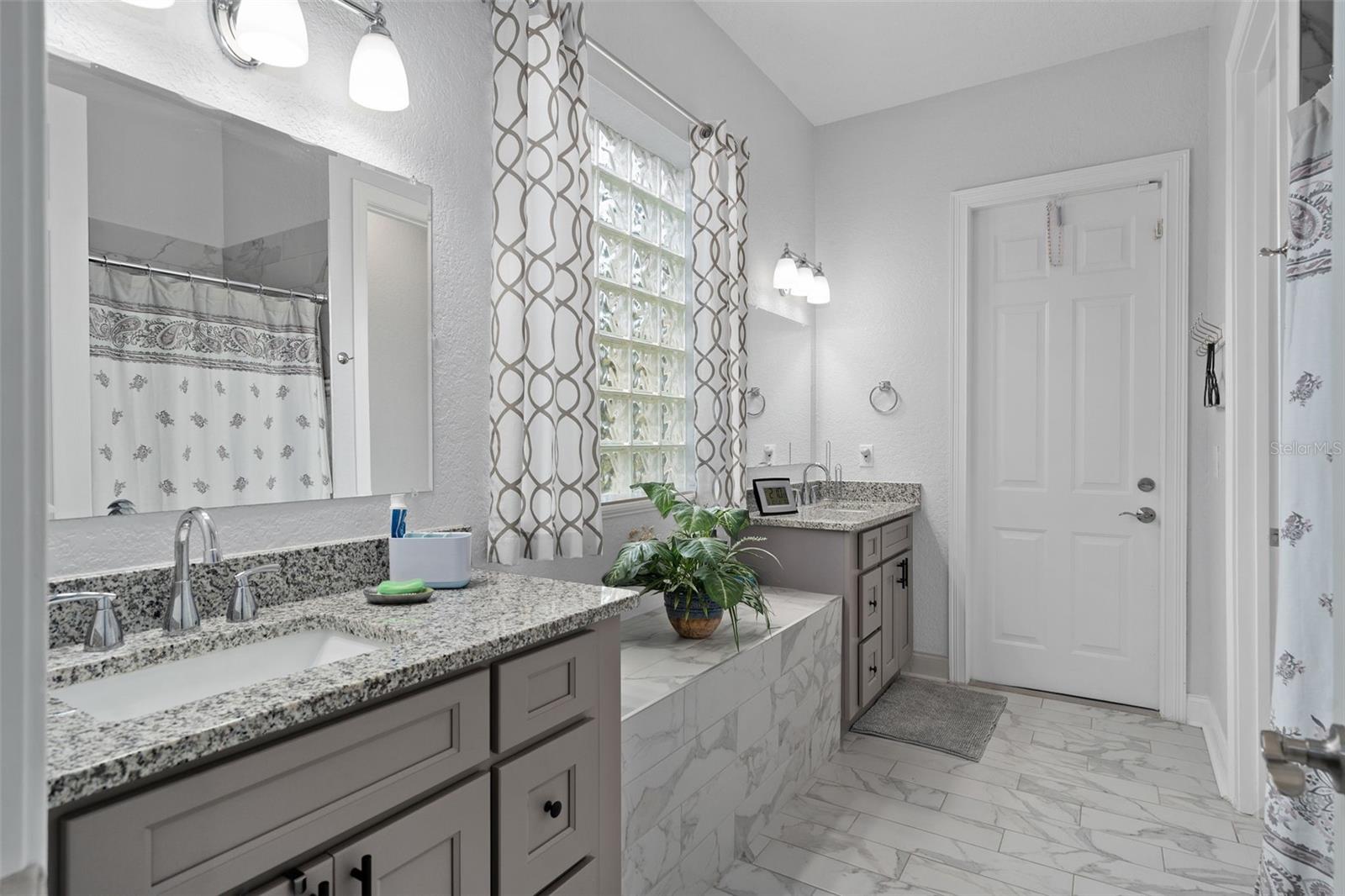 Downstairs Primary Bath fully upgraded with all new his/hers vanities and custom floor tile. Also has a door leading to the rear of the home.