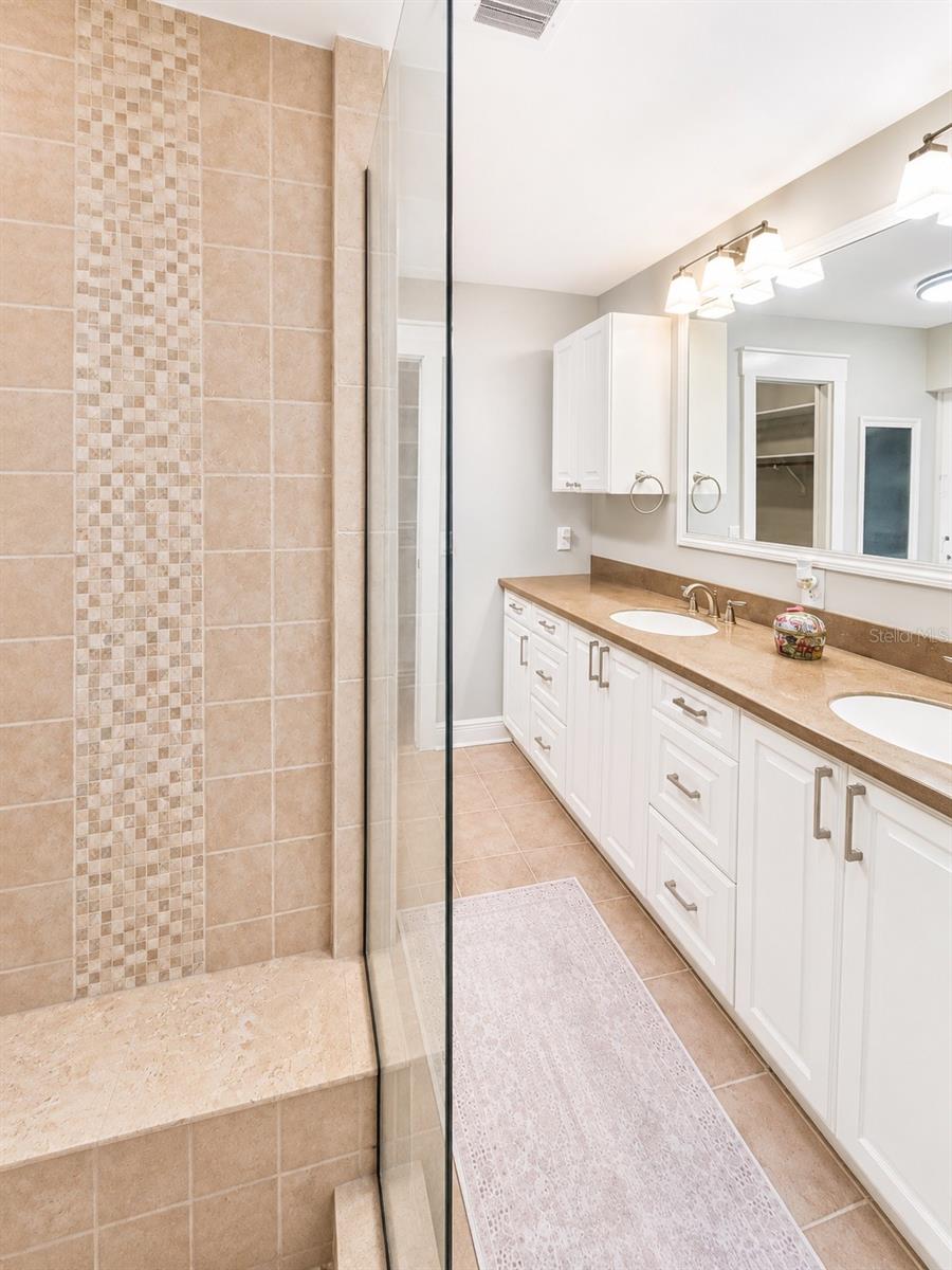 Private primary bath with a spacious tiled shower, custom built-in bench, long dual vanity, and a clean spa-like feel.