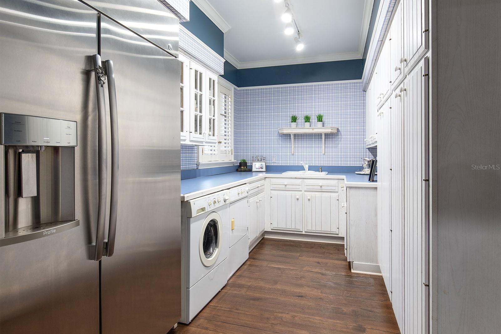 Look at the size of this laundry room! Situated off the corridor of the side entrance.  Equipped with an additional refrigerator, load of cabinetry and plenty of counter space for folding clothes and storage.