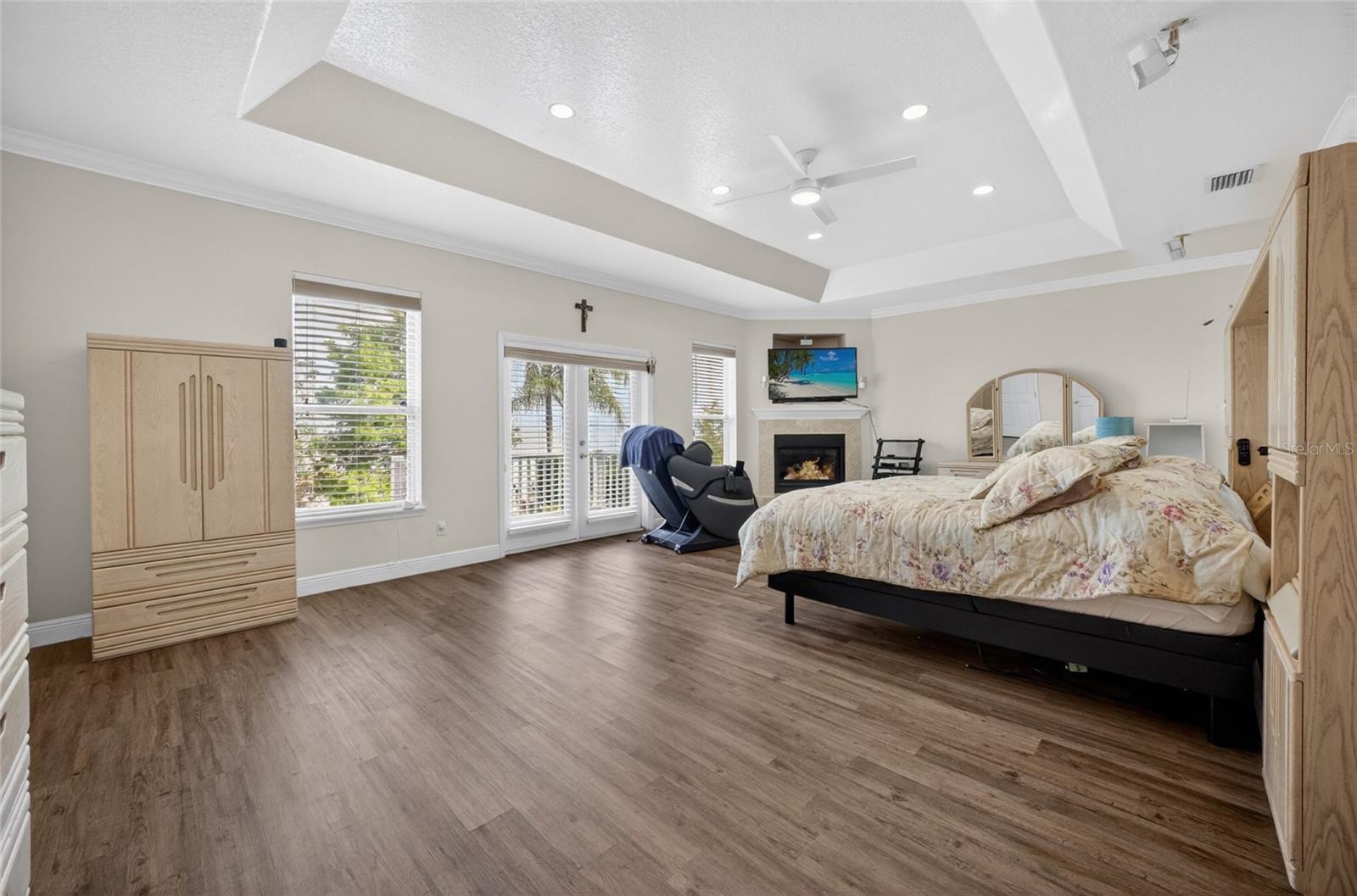 Primary bedroom upstairs with tray ceiling, corner fireplace and ensuite bath. French doors lead to the balcony overlooking the lake and pool area