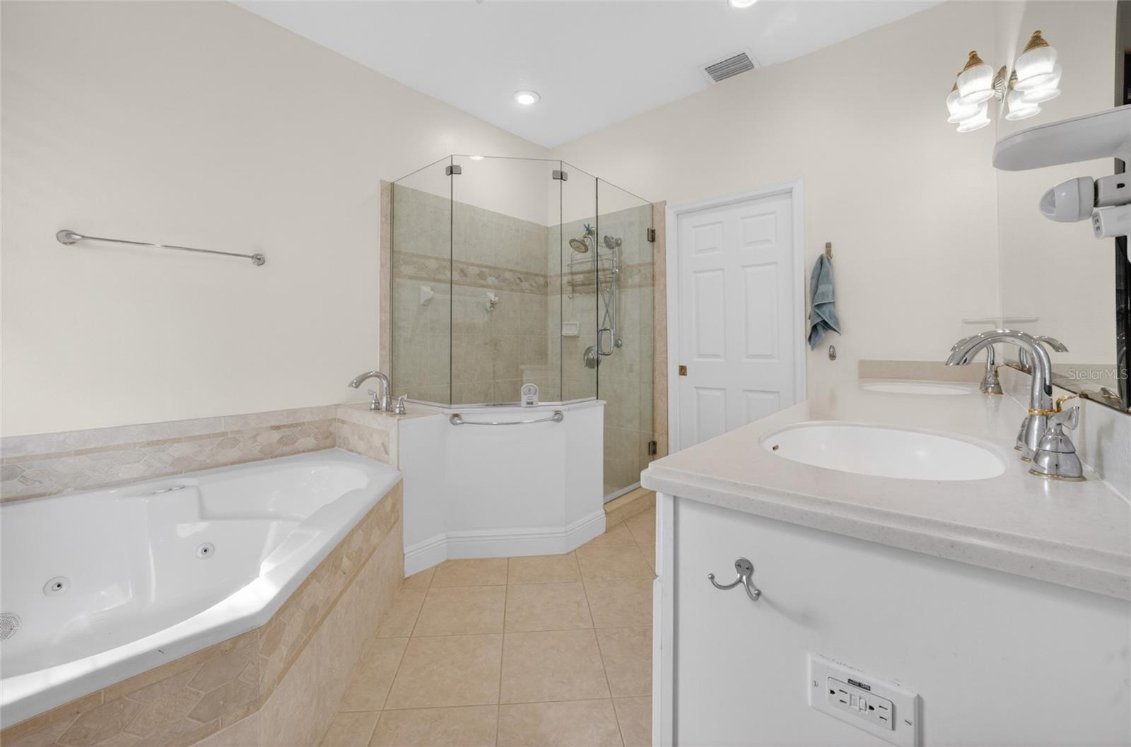 Primary bath with dual sinks, jacuzzi tub, shower and white vanity cabinet