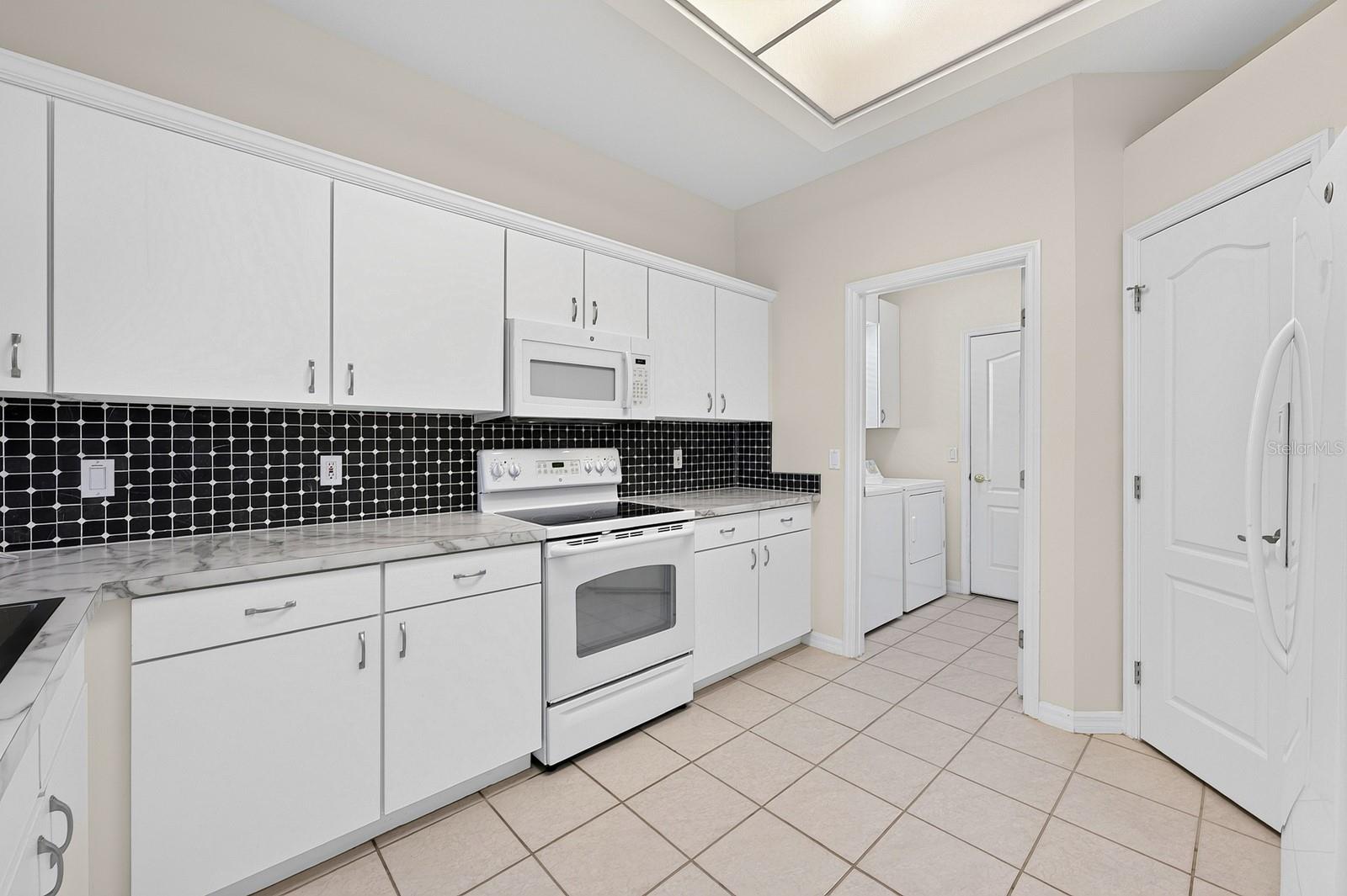 The spacious Kitchen, REFRESHED IN 2024, offers plenty to appreciate, including newer countertops, updated cabinet hardware and crown molding, a newer large sink and a tile backsplash.