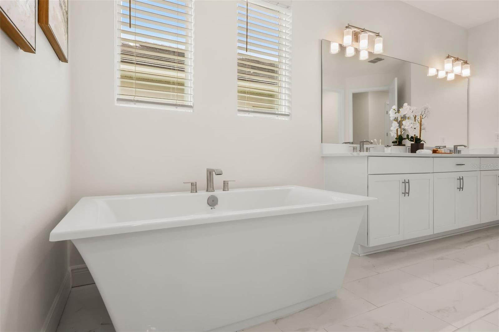 Luxurious primary bathroom with shower, dual vanity, soaker tub, and water closet