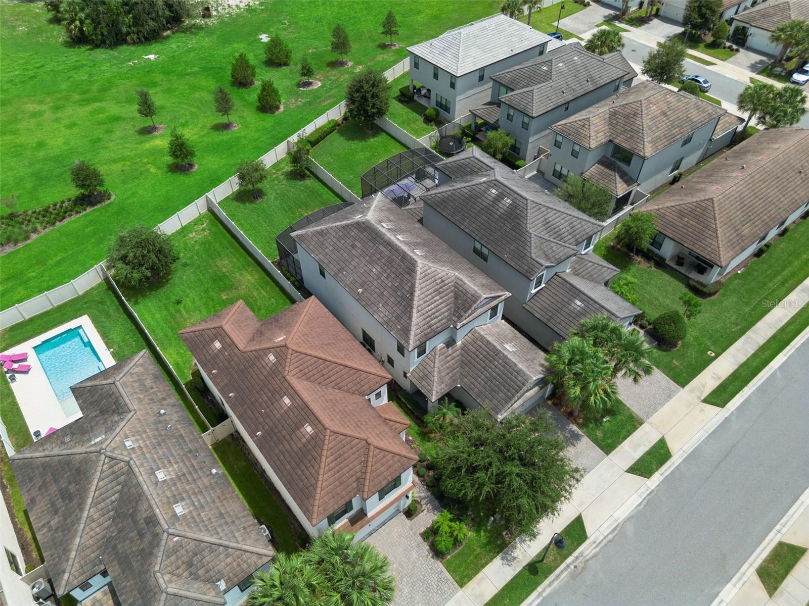 Overhead perspective highlights the home's two-story footprint, screened patio, fenced yard, and relationship to the surrounding green space.