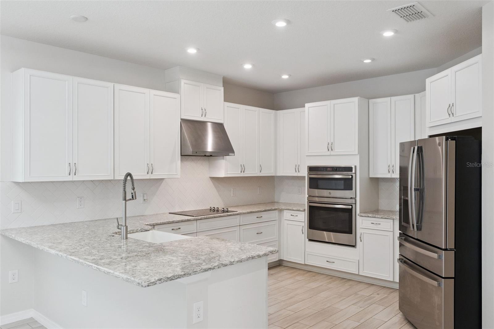 Kitchen  Bright kitchen features abundant white cabinetry, granite countertops, a tile backsplash, recessed lighting, stainless steel appliances, double wall ovens, and generous counter space for everyday prep.