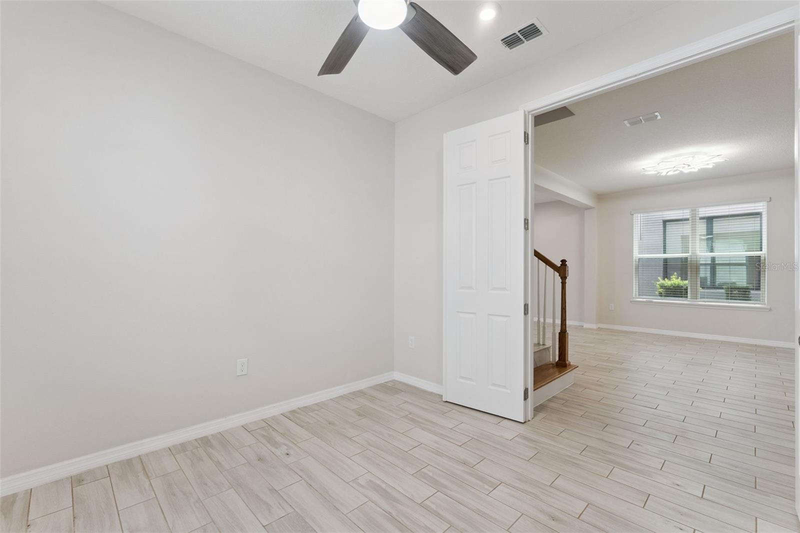 Downstairs Study  Bright, versatile main-level study with neutral finishes, tile flooring, a ceiling fan, and natural light, offering flexible space for a home office, reading room, or creative workspace.