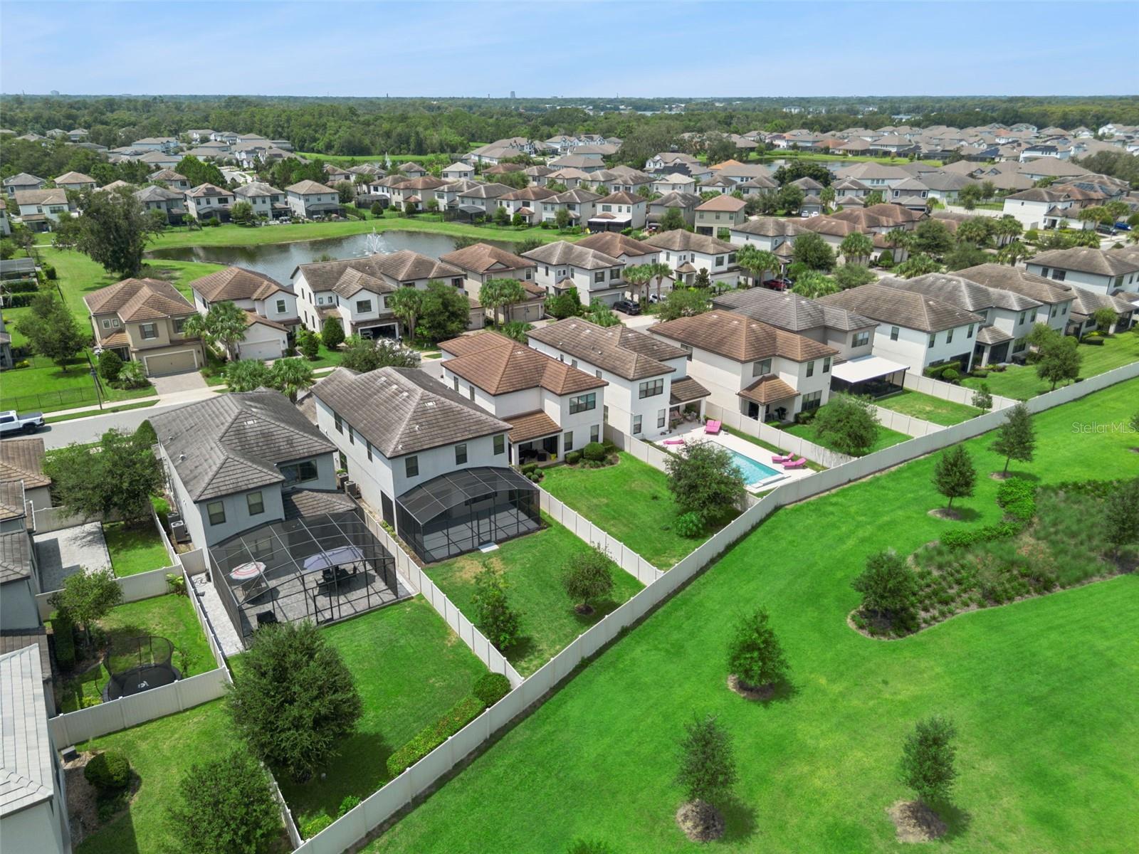 Aerial view captures the surrounding residential setting, nearby pond, and extensive landscaped green areas throughout the community.