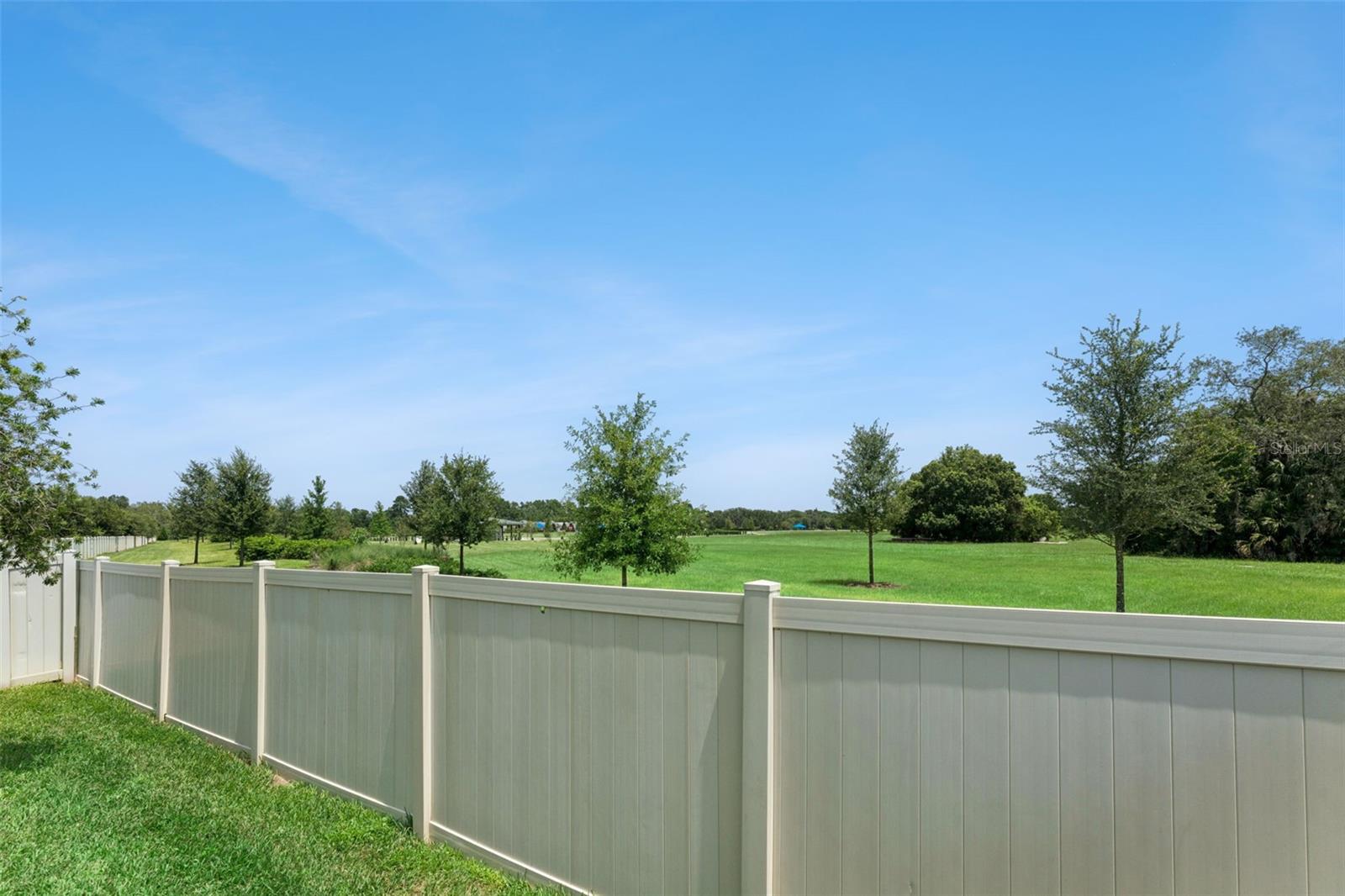 Fenced Backyard  The backyard enjoys an open outlook beyond the rear fence, with expansive maintained green space and mature trees in view.