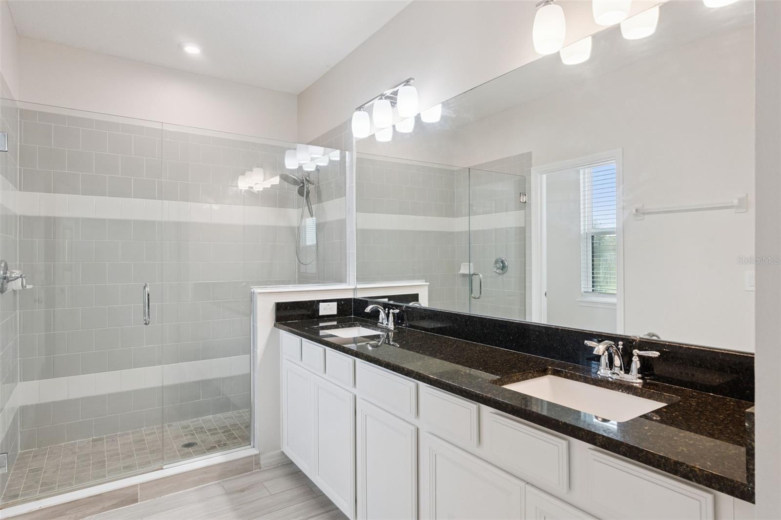Primary Bathroom  Primary bath showcases a large glass-enclosed tiled shower alongside the dual-sink vanity, creating a bright and functional ensuite retreat.