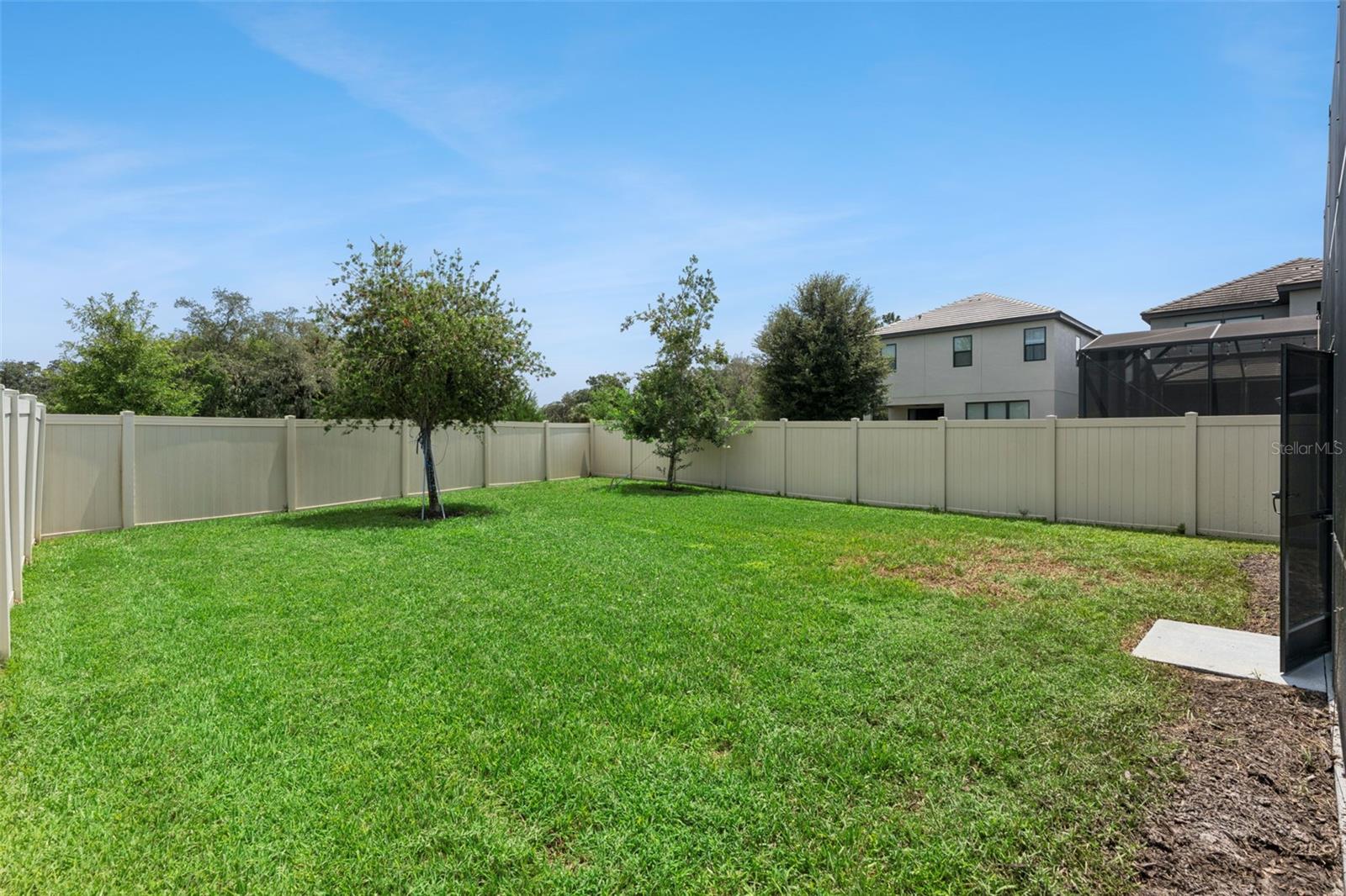 Fenced Backyard  Wide backyard view highlights the open lawn, established trees, and privacy fencing around the property.