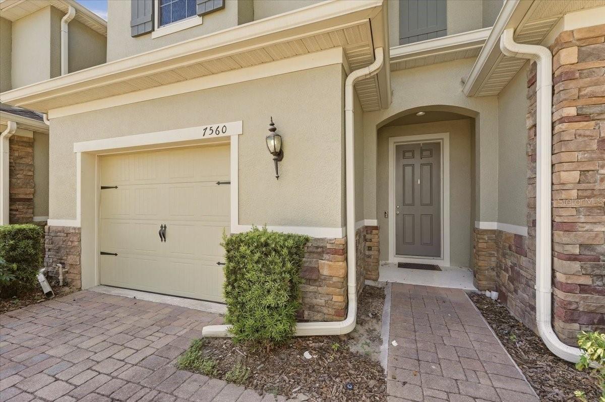 Welcoming entryway with stone detail, covered walkway, and attached one-car garage