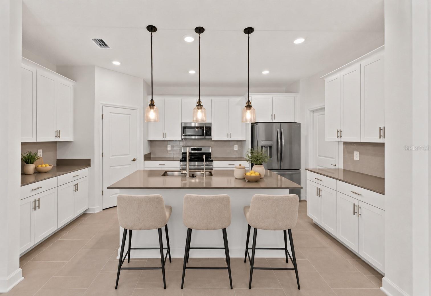 At the heart of the home, the kitchen features shaker style cabinetry, quartz countertops, stainless steel appliances, a tiled backsplash, pantry storage and a large island with breakfast bar seating beneath pendant lighting.