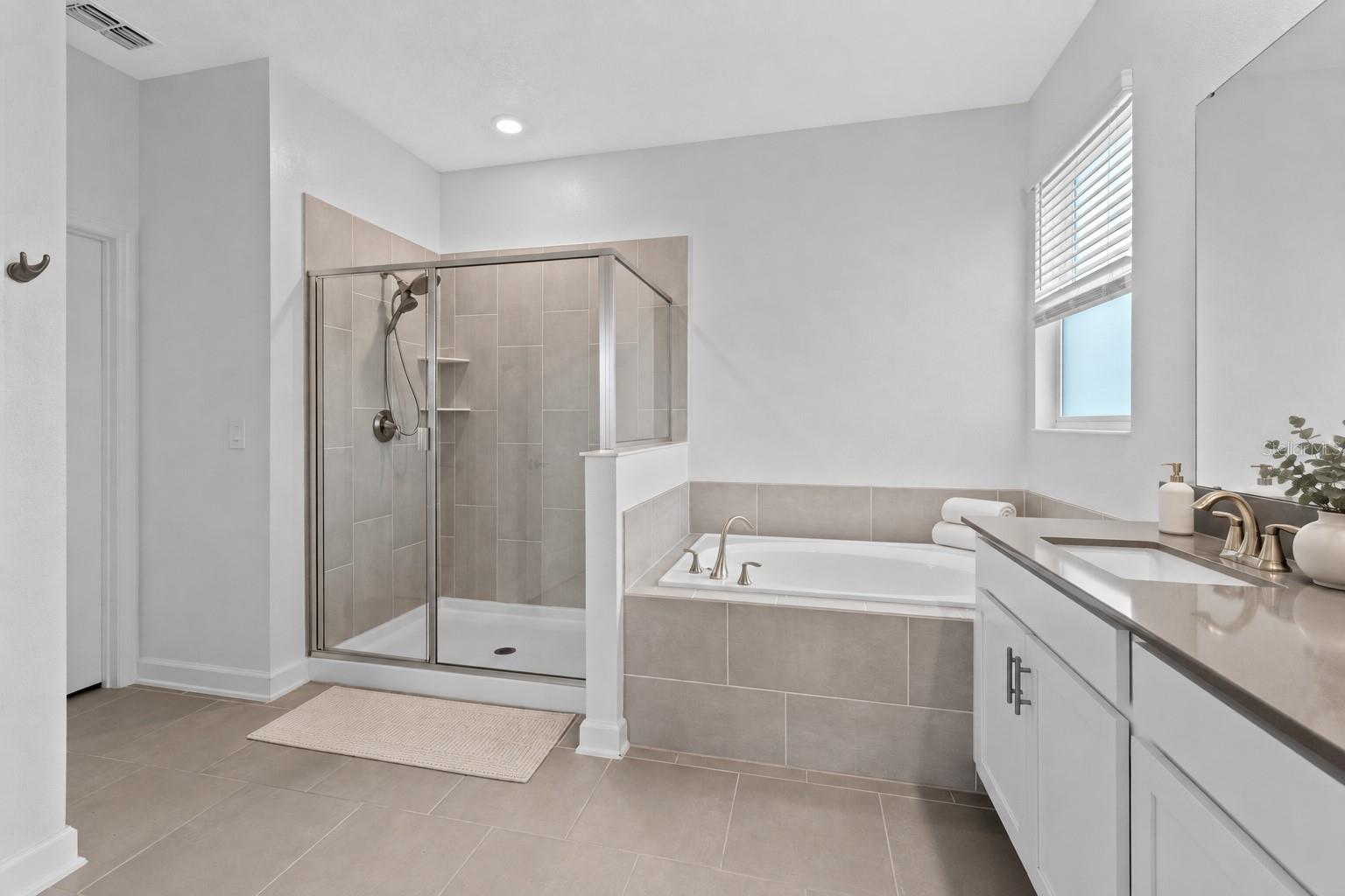 Tucked away at the rear of the home, the primary suite offers a generous walk in closet and a spacious private bathroom complete with quartz countertops, dual sinks, a soaking tub and separate shower. Direct access from the primary suite into the laundry room adds another layer of everyday convenience.