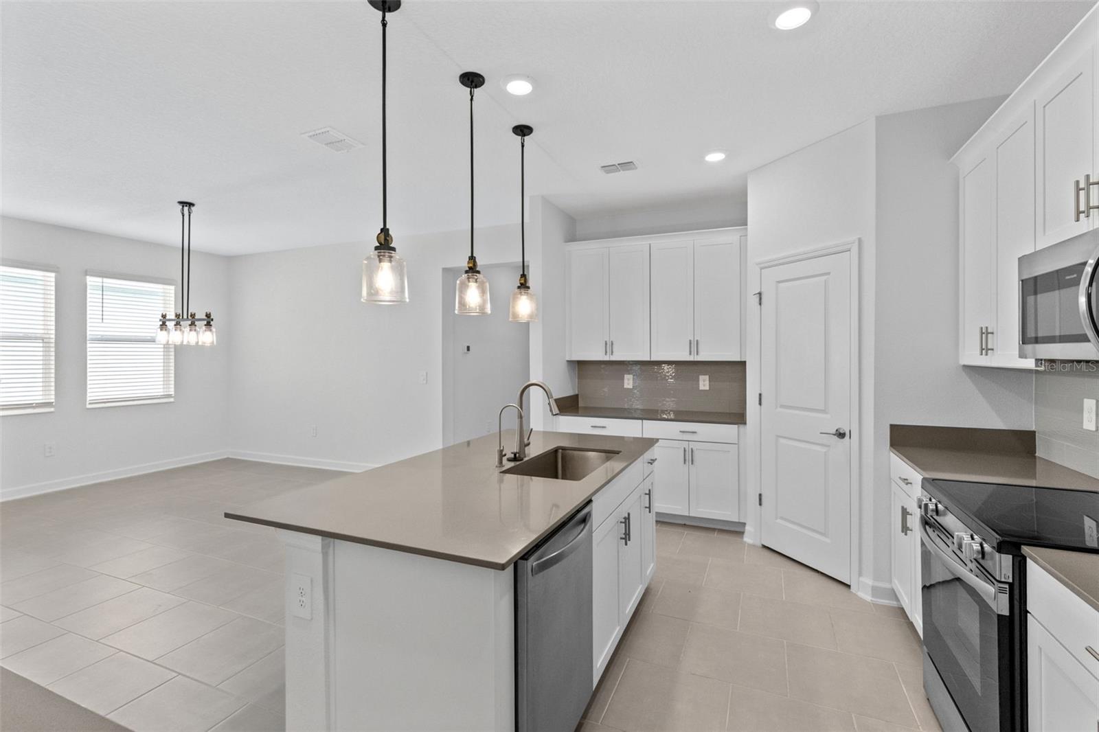 At the heart of the home, the kitchen features shaker style cabinetry, quartz countertops, stainless steel appliances, a tiled backsplash, pantry storage and a large island with breakfast bar seating beneath pendant lighting.