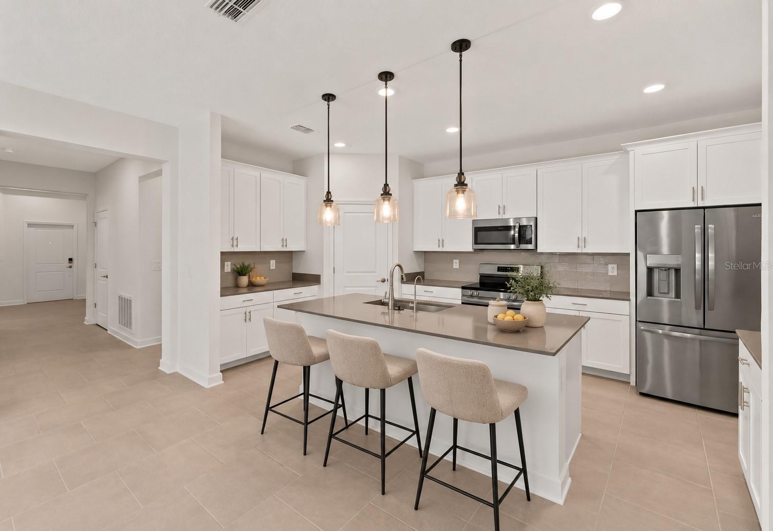 At the heart of the home, the kitchen features shaker style cabinetry, quartz countertops, stainless steel appliances, a tiled backsplash, pantry storage and a large island with breakfast bar seating beneath pendant lighting.