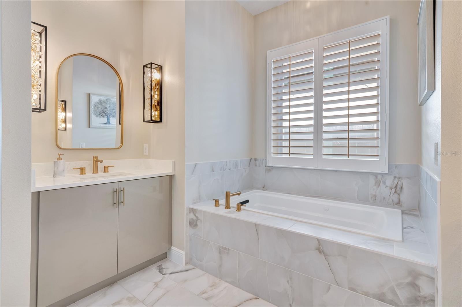 Elegant bathroom featuring a soaking tub, upgraded tile surrounds and a vanity accented by designer sconces.