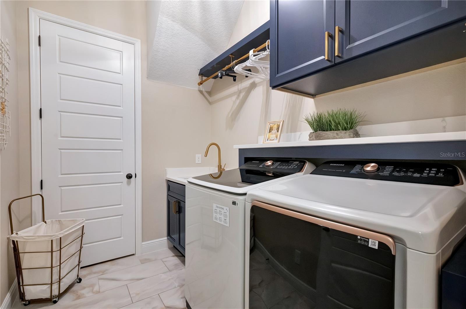 Custom laundry room featuring upgraded cabinetry, a utility sink, hanging rack and countertop above the washer and dryer.