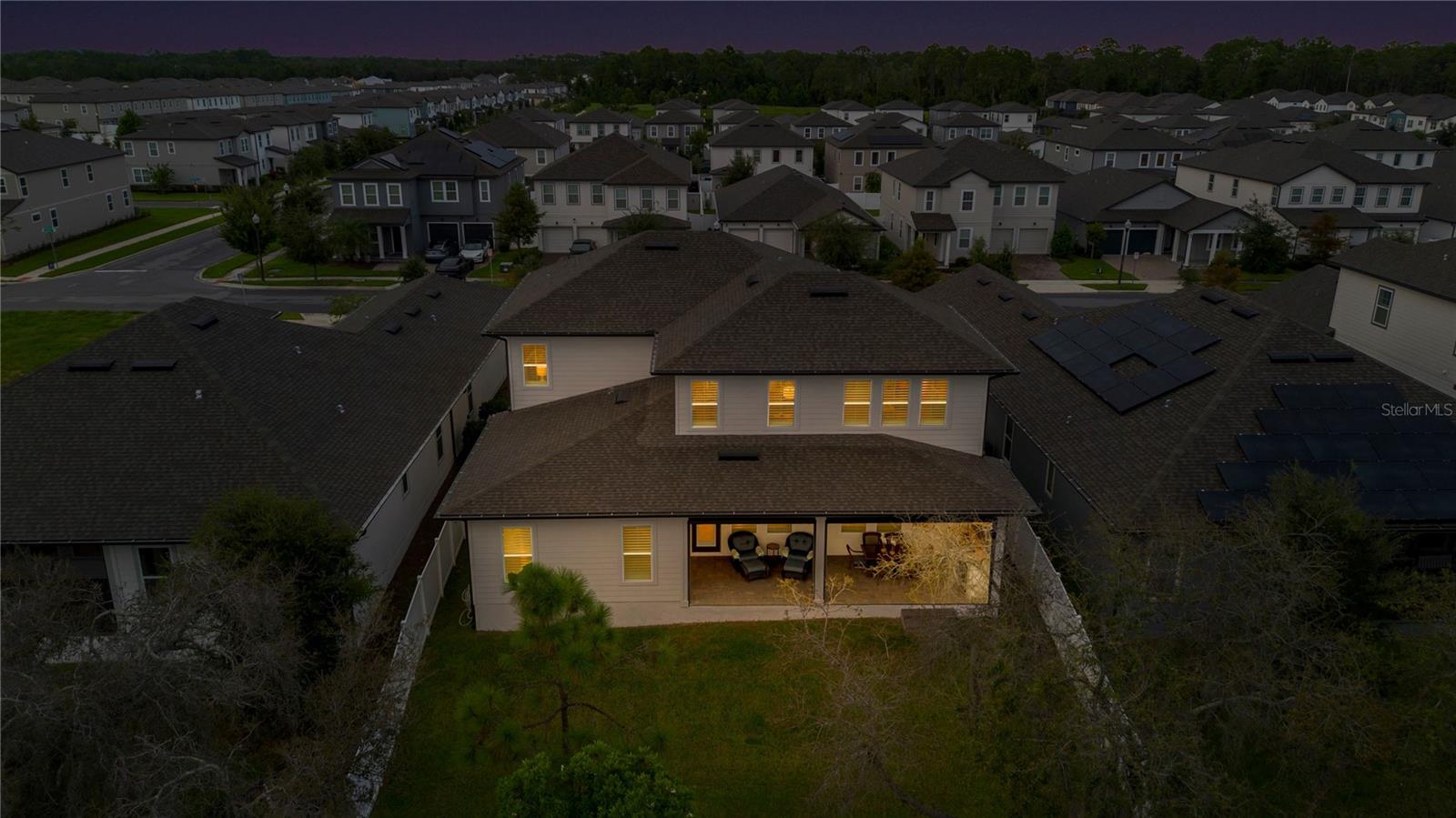 Rear aerial at twilight captures the backyard and warmly illuminated covered lanai.