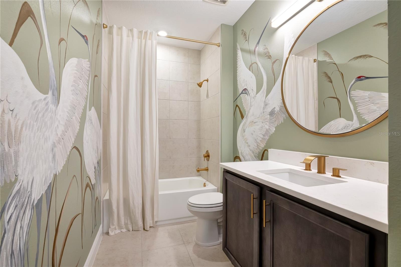 Beautifully styled bathroom featuring a bird-pattern accent wall, upgraded vanity and tub with shower.