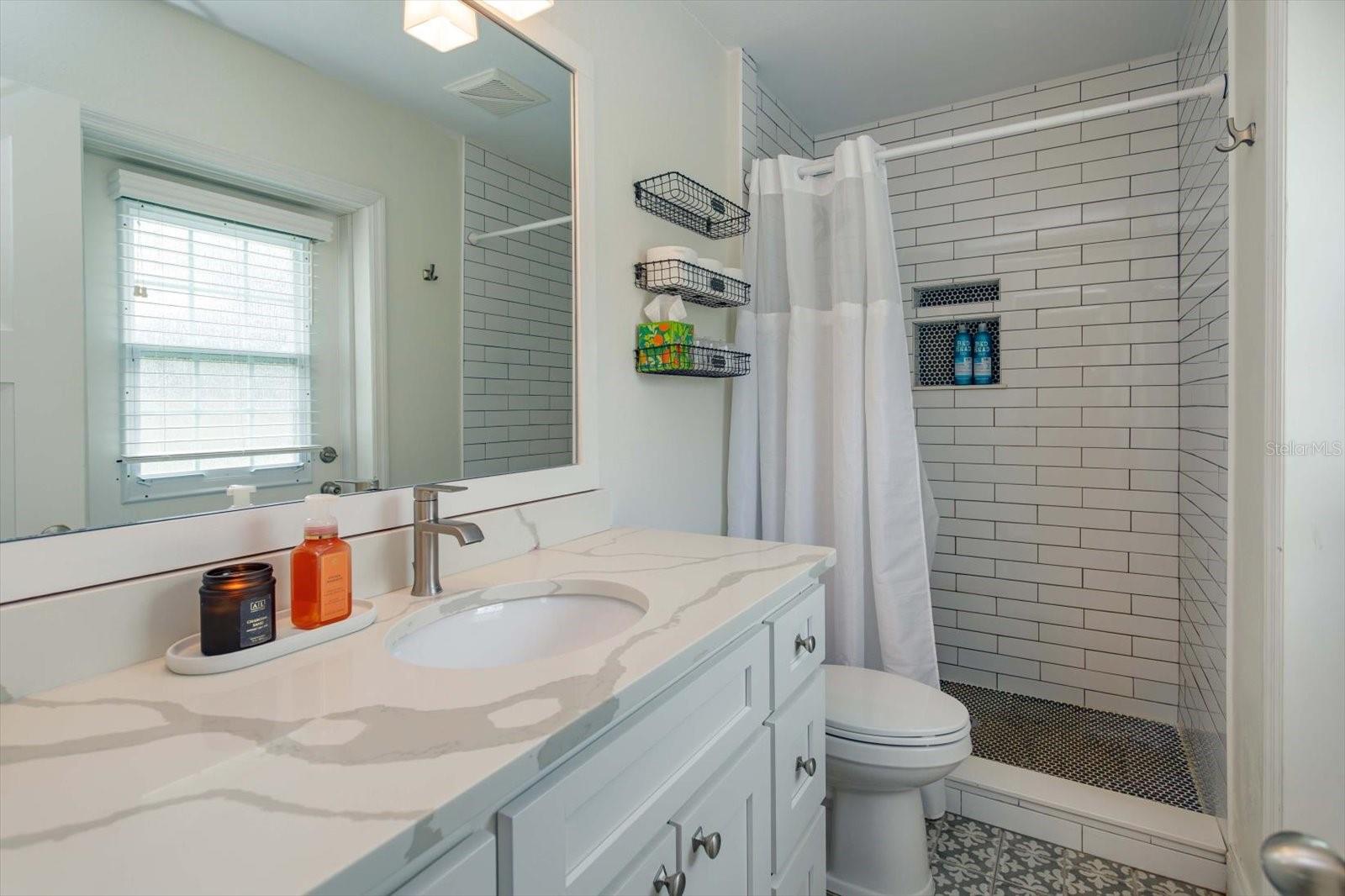Renovated primary shower with shaker vanity, stone counter, new lighting and fixtures
