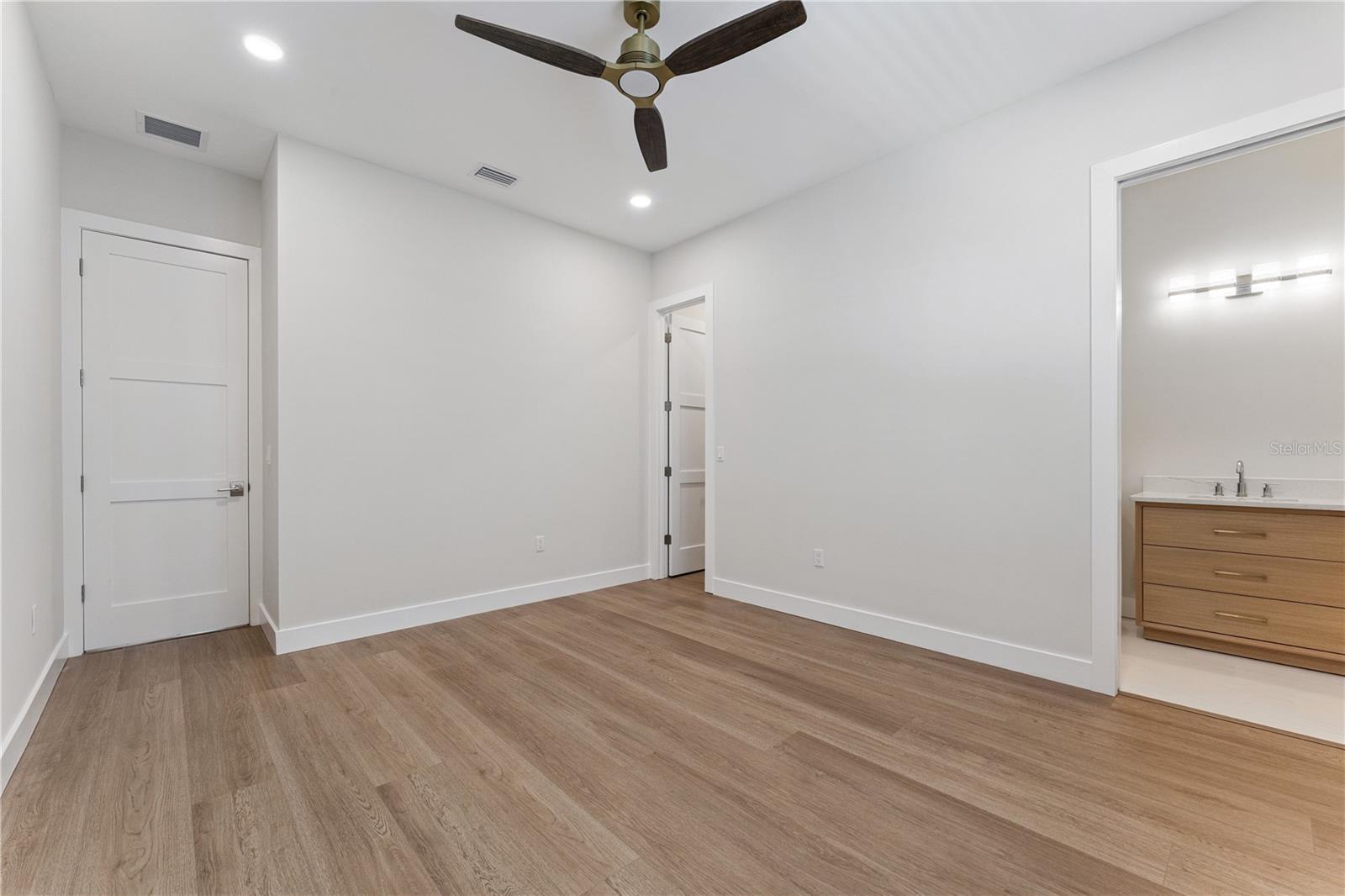 This bedroom includes a shuttered window, ceiling fan, and a view into the built-in closet.