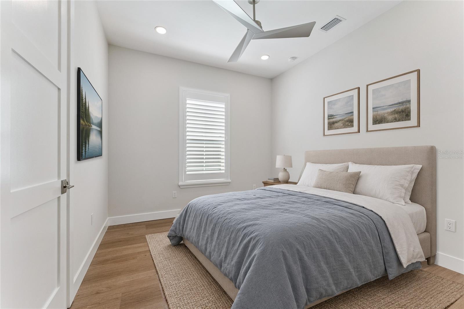 Virtually Staged - This bedroom features a white ceiling fan, shuttered window, and light finishes.