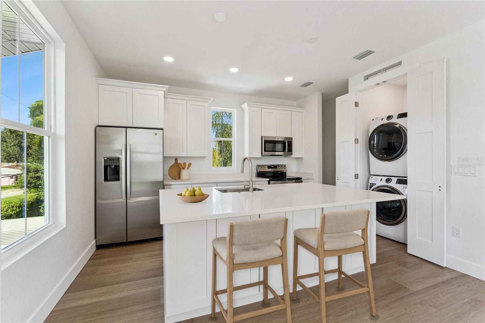 Virtually Staged - The guest-suite kitchen includes a white island, stainless steel appliances, and a stacked washer and dryer.