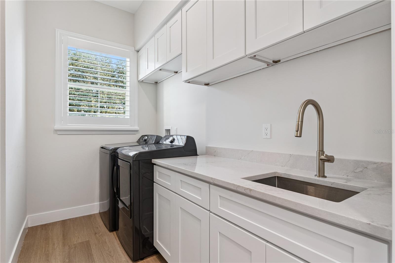 The laundry room includes a washer, dryer, utility sink, and upper and lower cabinetry.