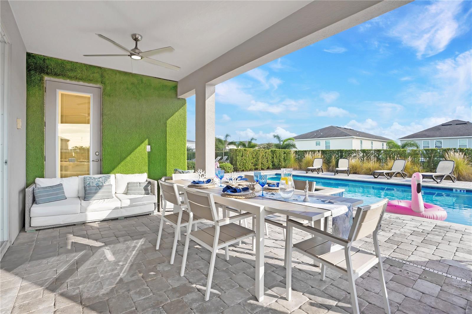 A spacious covered lanai with ceiling fans, outdoor dining, and poolside views