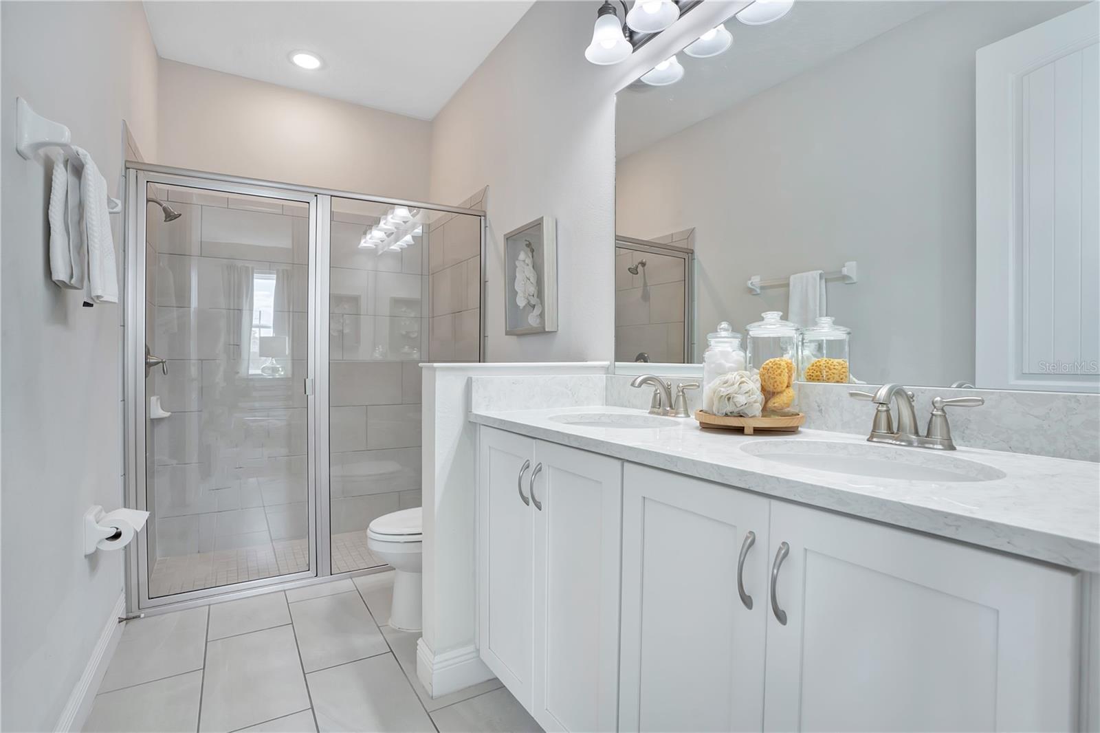Bright, elegant en-suite bath to 1st floor primary with a glass-enclosed shower and generous vanity
