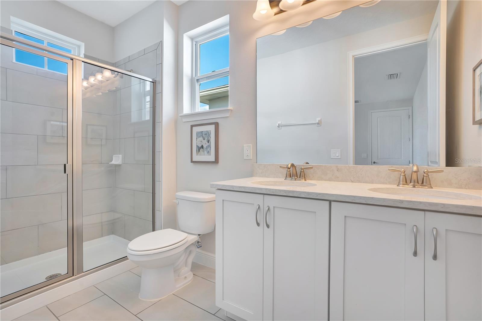 A beautifully appointed en-suite bath to upstairs primary with a spacious vanity and glass-enclosed shower