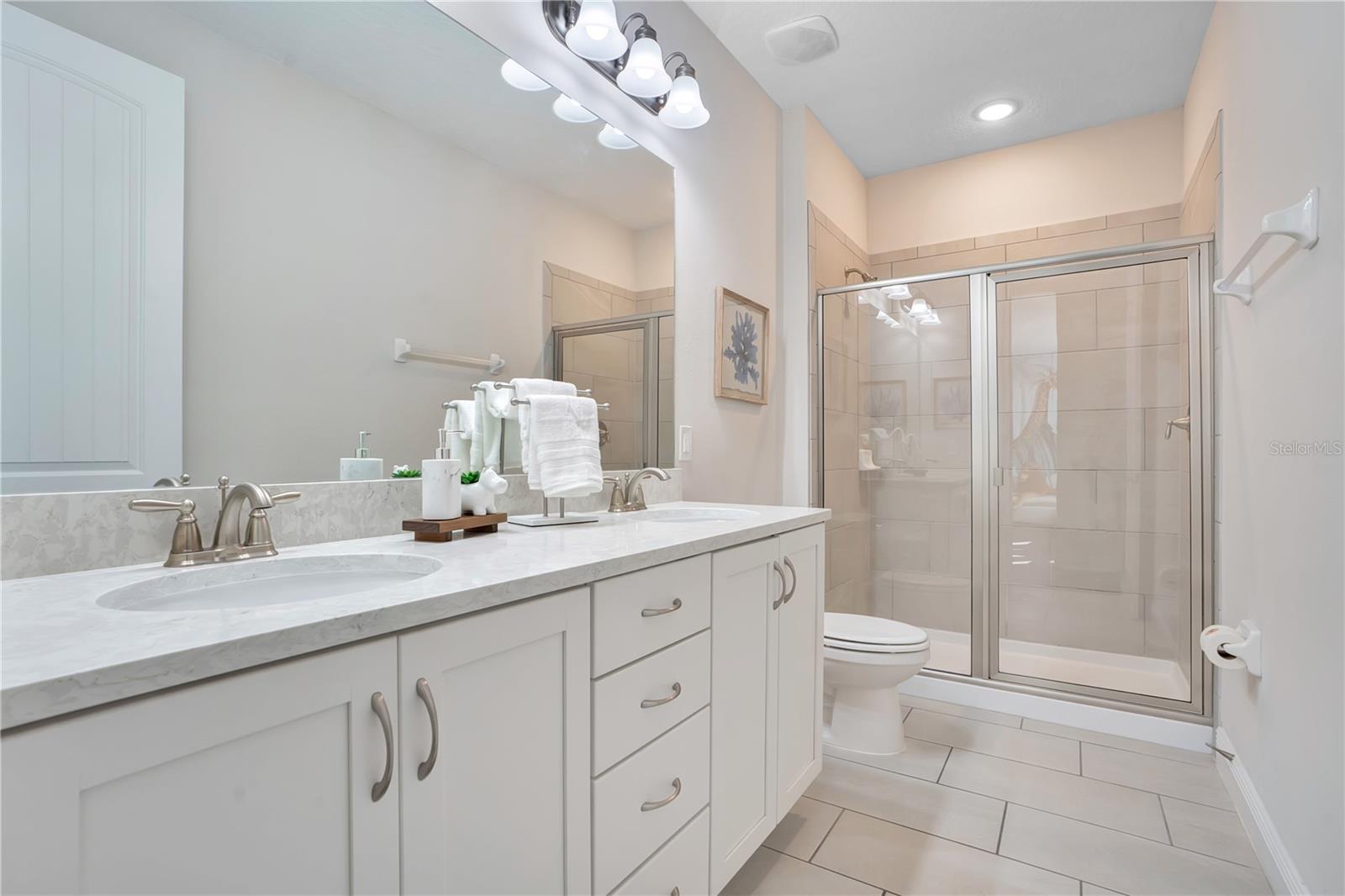 A beautifully finished bath with generous counter space and a glass-enclosed shower -