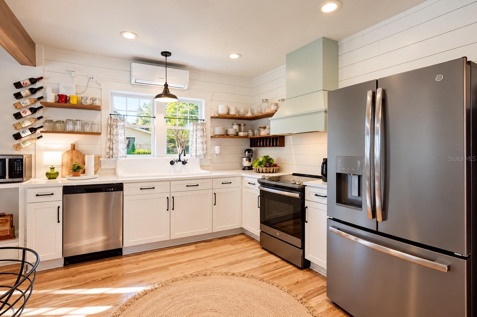 FARMHOUSE-STYLE KITCHEN featuring white shaker cabinetry, shiplap walls, floating wood shelves, gorgeous wood flooring, stainless steel appliances, and an OVERSIZED FARMHOUSE APRON-FRONT SINK with wall-mounted faucet beneath sun-filled windows overlooking the lush backyard, filled with an abundance of EDIBLE TREES, PLANTS, AND HERBS, offering a wonderful opportunity to embrace FARM-TO-TABLE LIVING RIGHT IN YOUR OWN BACKYARD! FARMHOUSE-STYLE KITCHEN featuring white shaker cabinetry, shiplap walls, floating wood shelves, gorgeous wood flooring, stainless steel appliances, and an OVERSIZED FARMHOUSE APRON-FRONT SINK with wall-mounted faucet beneath sun-filled windows overlooking the lush backyard, filled with an abundance of EDIBLE TREES, PLANTS, AND HERBS, offering a wonderful opportunity to embrace FARM-TO-TABLE LIVING RIGHT IN YOUR OWN BACKYARD!