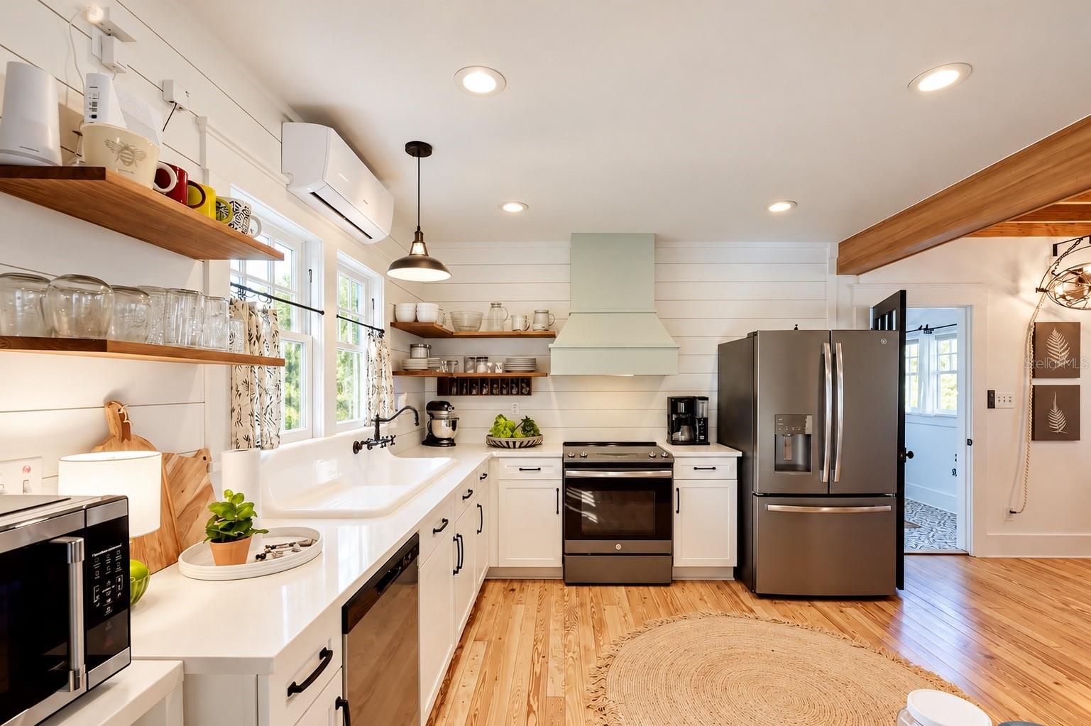Updated FARMHOUSE-STYLE KITCHEN featuring white cabinetry, shiplap walls, gorgeous wood flooring, floating wood shelves, a charming OVERSIZED FARMHOUSE APRON-FRONT SINK beneath sun-filled windows, stainless steel appliances, and a stylish range hood! Updated FARMHOUSE-STYLE KITCHEN featuring white cabinetry, shiplap walls, gorgeous wood flooring, floating wood shelves, a charming OVERSIZED FARMHOUSE APRON-FRONT SINK beneath sun-filled windows, stainless steel appliances, and a stylish range hood!