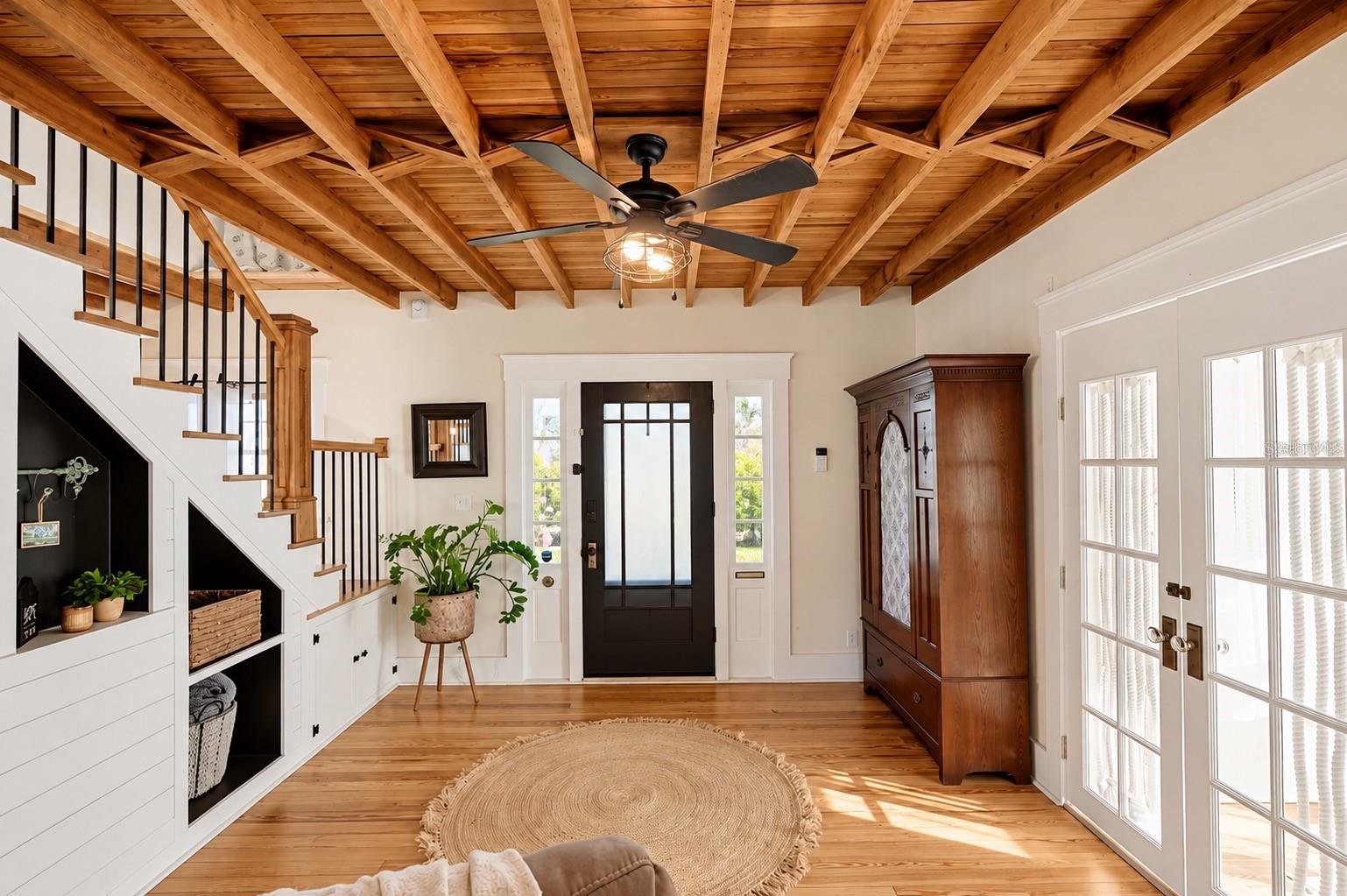 CHARMING ENTRYWAY featuring stunning EXPOSED WOOD BEAM CEILINGS, beautiful hardwood floors, a wooden staircase with black iron balusters, custom built-in shelving and storage, and French doors that fill the space with natural light. CHARMING ENTRYWAY featuring stunning EXPOSED WOOD BEAM CEILINGS, beautiful hardwood floors, a wooden staircase with black iron balusters, custom built-in shelving and storage, and French doors that fill the space with natural light.