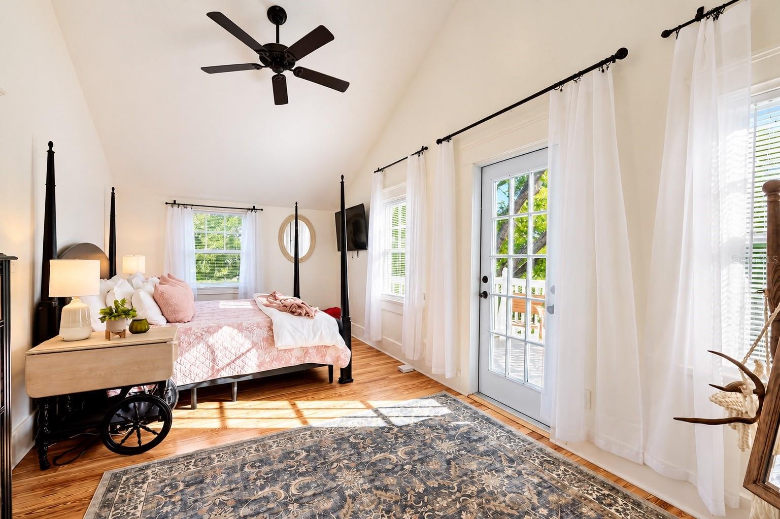 Bright and spacious bedroom featuring vaulted ceilings, beautiful hardwood floors, abundant natural light, and French doors leading to the outdoor deck.