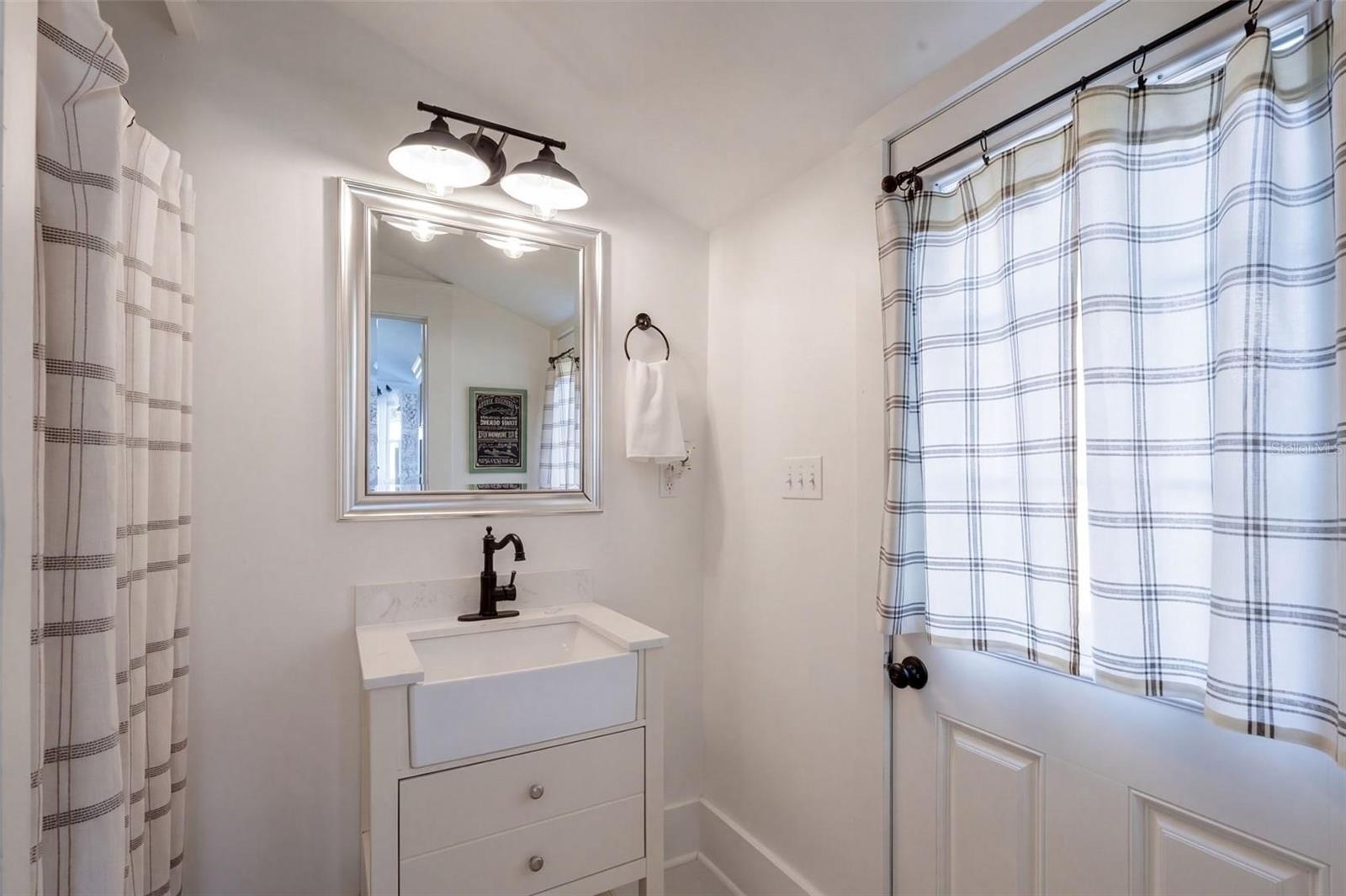 UPDATED FULL DOWNSTAIRS BATHROOM featuring a charming farmhouse-style vanity, stylish black fixtures, and modern lighting. Convenient exterior door provides direct access to the spacious FENCED BACKYARD AND BARN, perfect for enjoying the property's outdoor living spaces!
