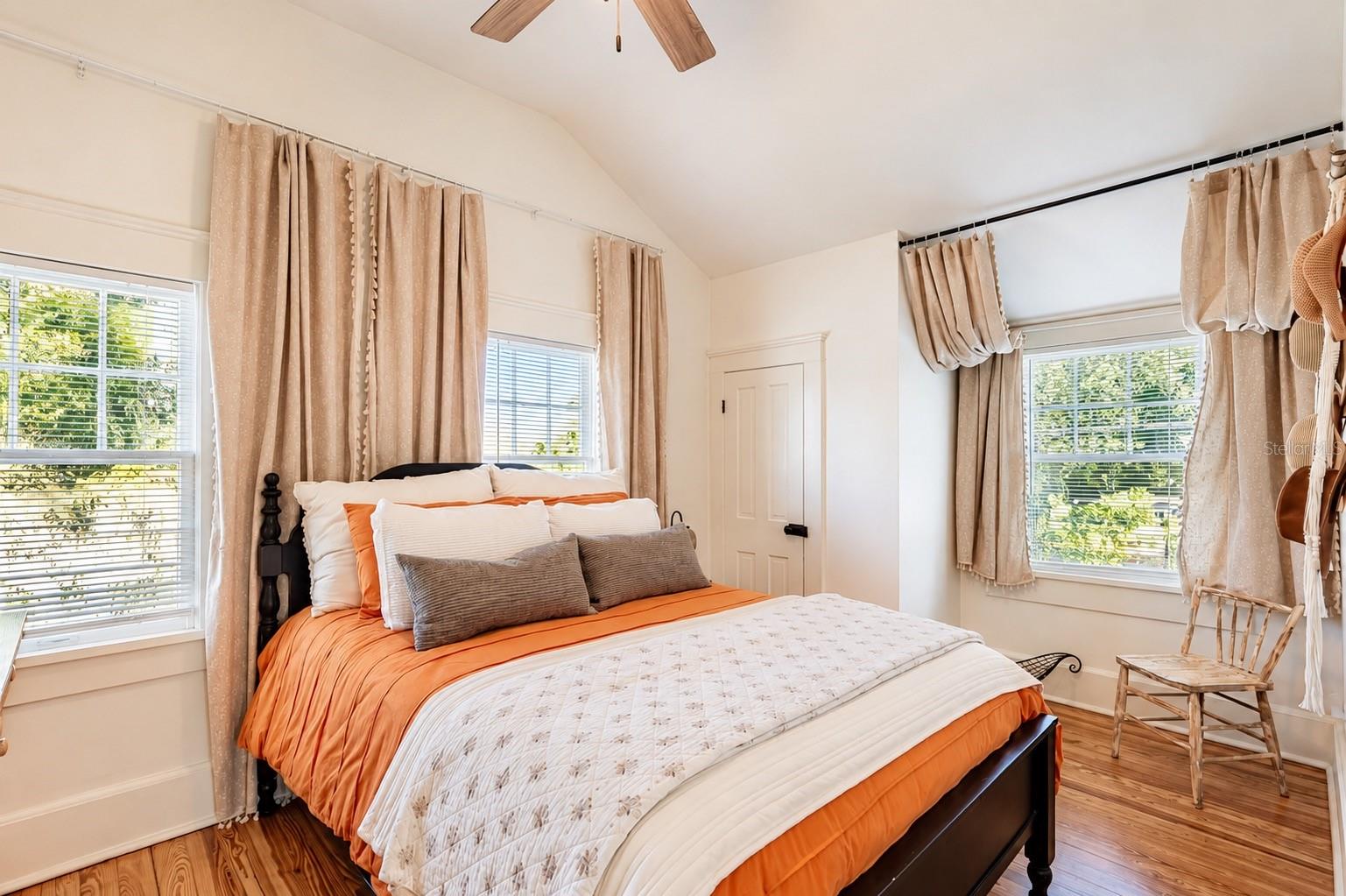 Bright and inviting SECOND BEDROOM UPSTAIRS featuring vaulted ceilings, beautiful wood flooring, abundant natural light, ceiling fan, and a WALK-IN CLOSET.