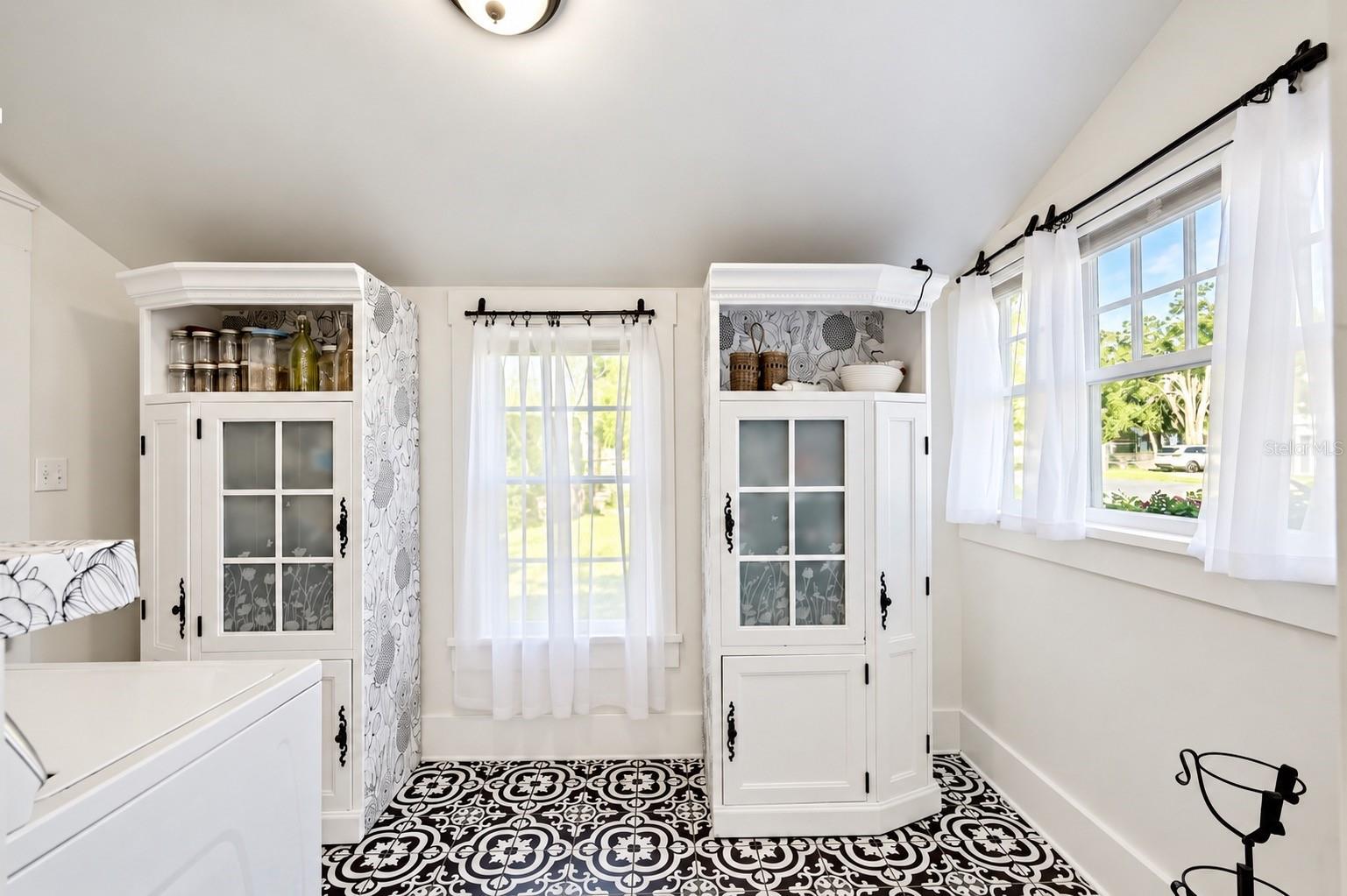 INDOOR LAUNDRY ROOM featuring beautiful patterned tile flooring, abundant natural light, and decorative storage cabinets. Convenient access through the adjoining full downstairs bathroom leads to the spacious FENCED BACKYARD AND BARN, offering both functionality and farmhouse charm!