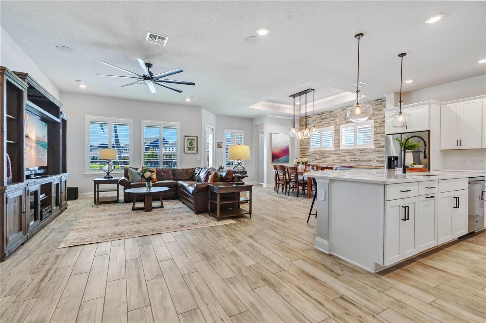 Open floor plan connecting the great room, kitchen, and dining area. Wood look plank tile, crown moulding, and natural light throughout this one story Lake Nona home.