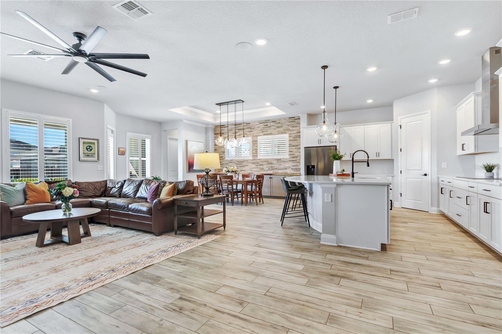 Bright great room open to the kitchen with high ceilings, ceiling fan, and plantation shutters. Easy everyday living in Laureate Park, Lake Nona.