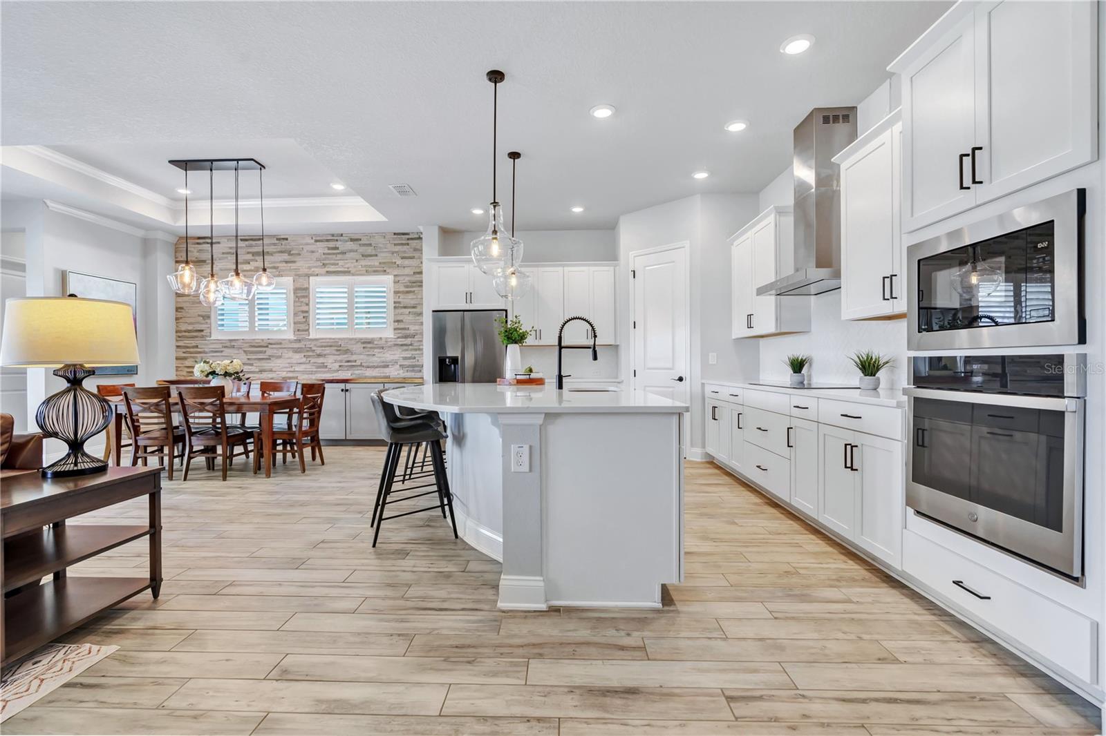 Kitchen view from the great room showing the oversized quartz island, 42 inch cabinetry, wall oven, and microwave.