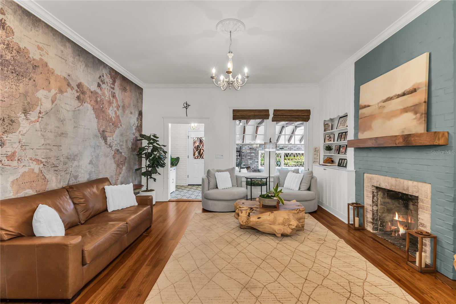 The warm and welcoming Formal Living Room is anchored by a wood-burning brick fireplace accented by a substantial wood mantle and custom painted brick. A custom built in shelf, original wood flooring and chandelier preserve the homes original historic charm and a world map accent wall adds personality. The spacious layout offers a seamless connection to the adjoining dining room and kitchen, creating an effortless flow throughout the home's main living spaces.