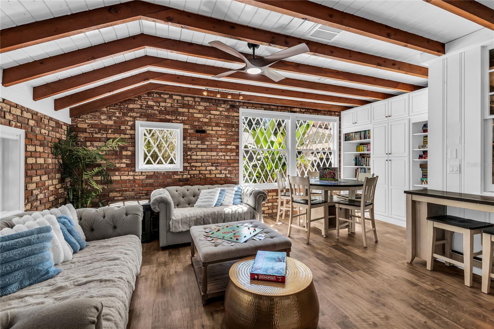 Natural light pours into the spacious family room that features warm brick walls, exposed wood beams and distinctive diamond-pane windows that create a timeless architectural backdrop.