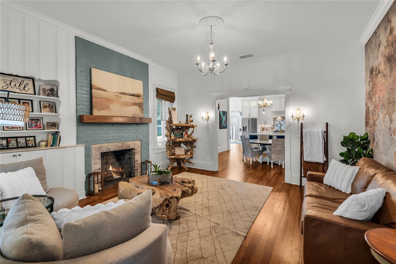 The warm and welcoming Formal Living Room is anchored by a wood-burning brick fireplace accented by a substantial wood mantle and custom painted brick. A custom built in shelf, original wood flooring and chandelier preserve the homes original historic charm and a world map accent wall adds personality. The spacious layout offers a seamless connection to the adjoining dining room and kitchen, creating an effortless flow throughout the home's main living spaces.